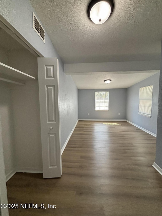 interior space with a textured ceiling, dark wood finished floors, visible vents, and baseboards