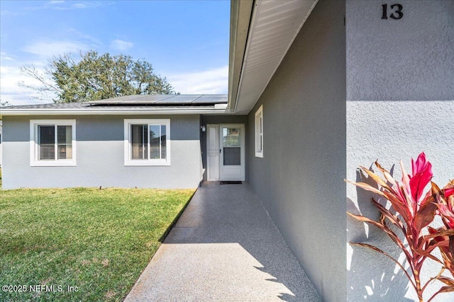 doorway to property featuring stucco siding, solar panels, and a yard