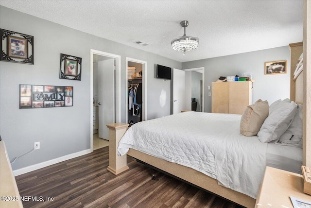 bedroom featuring dark wood-style floors, visible vents, a spacious closet, a textured ceiling, and baseboards