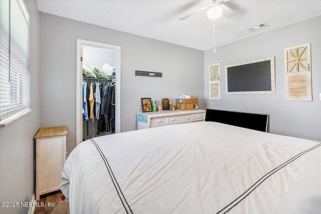 bedroom with a textured ceiling, dark wood-type flooring, visible vents, a spacious closet, and a closet