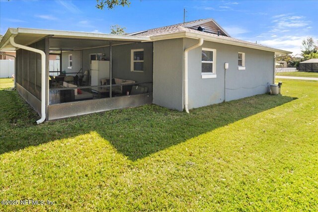 back of property featuring a sunroom, a lawn, and stucco siding