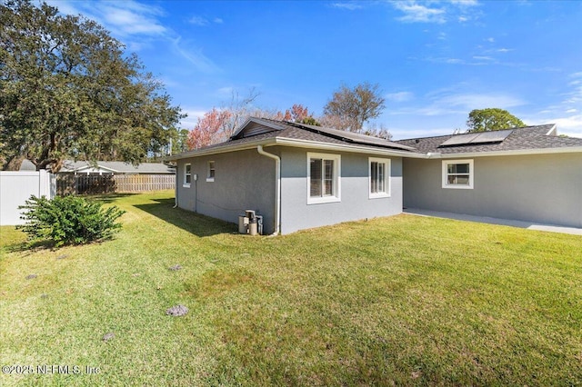 view of side of property with solar panels, stucco siding, a yard, and fence