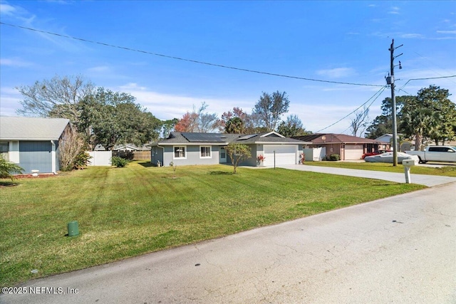 ranch-style home featuring solar panels, concrete driveway, an attached garage, fence, and a front lawn