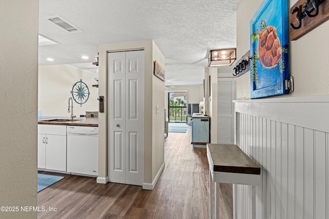 corridor featuring a sink, visible vents, a textured ceiling, and wood finished floors