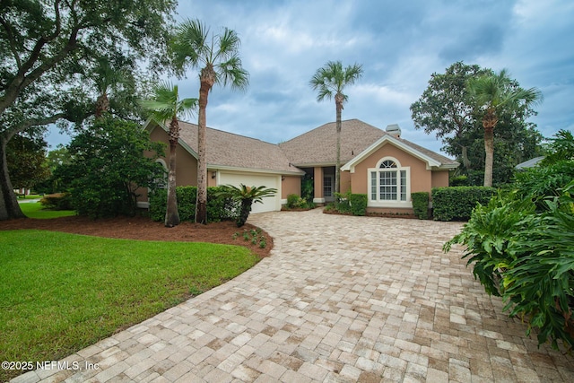 ranch-style home featuring a front lawn, decorative driveway, an attached garage, and stucco siding