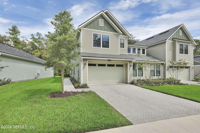 view of front of property featuring a garage, a shingled roof, decorative driveway, a front lawn, and board and batten siding