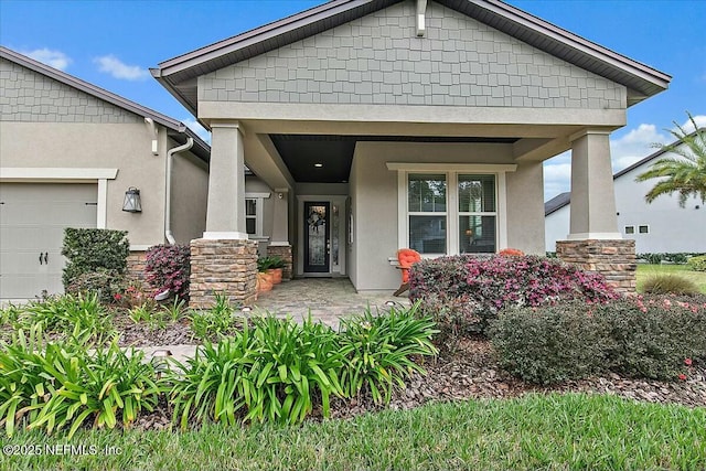 entrance to property with a porch, stone siding, an attached garage, and stucco siding