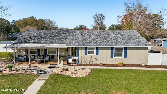 ranch-style house featuring covered porch, roof with shingles, fence, and a front yard