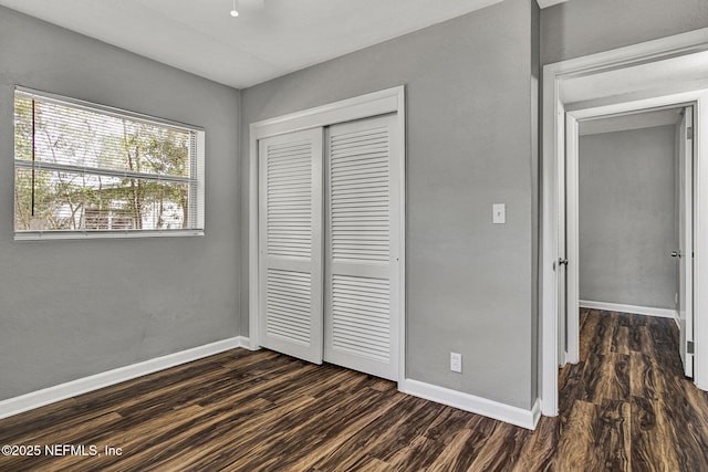 unfurnished bedroom featuring a closet, baseboards, and dark wood-style flooring