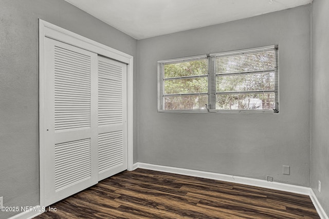 unfurnished bedroom with a closet, multiple windows, baseboards, and dark wood-type flooring