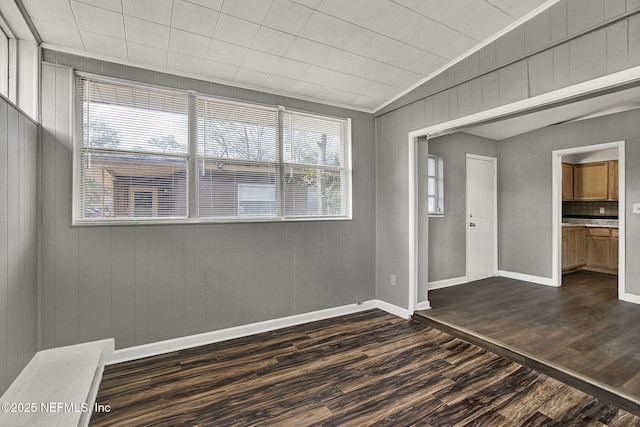 unfurnished room with lofted ceiling, dark wood finished floors, and baseboards