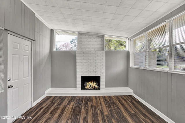 unfurnished living room featuring a fireplace, wooden walls, and wood finished floors