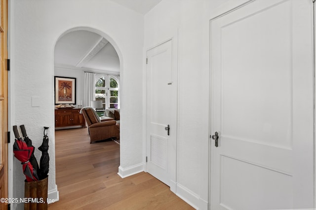 corridor with arched walkways, light wood finished floors, visible vents, and baseboards