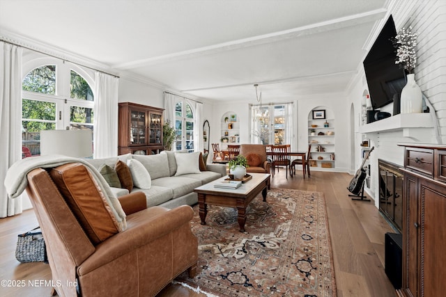 living room featuring built in shelves, beamed ceiling, light wood-type flooring, and crown molding