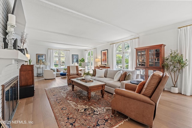 living room featuring beamed ceiling, a fireplace with flush hearth, and light wood-style floors