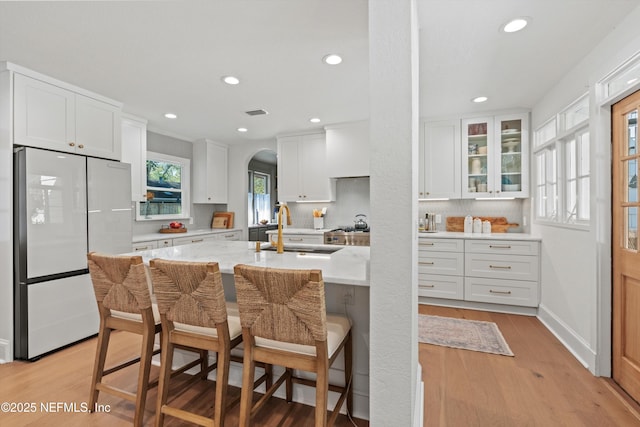 kitchen with arched walkways, light wood-style flooring, refrigerator, a sink, and white cabinets