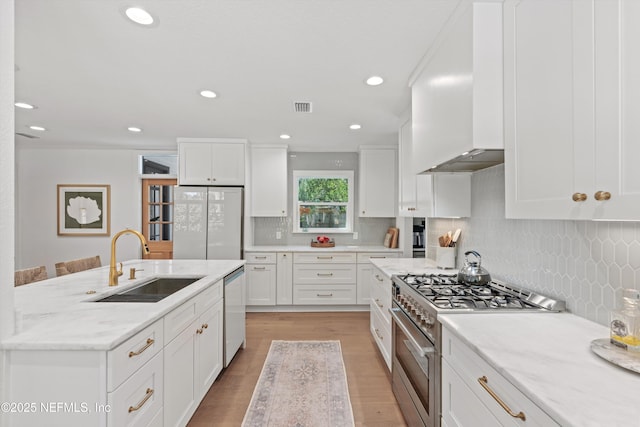 kitchen featuring white cabinetry, wall chimney exhaust hood, appliances with stainless steel finishes, and a sink