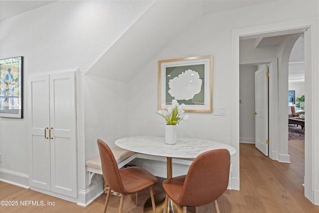 dining room featuring light wood finished floors, baseboards, arched walkways, lofted ceiling, and breakfast area