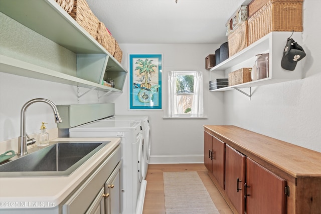 clothes washing area featuring washer and dryer, cabinet space, a sink, light wood-type flooring, and baseboards