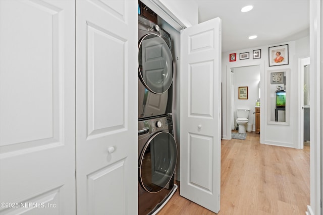 laundry area featuring laundry area, light wood-type flooring, stacked washing maching and dryer, and recessed lighting