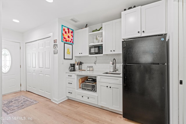 kitchen featuring open shelves, a sink, visible vents, light wood-type flooring, and black appliances