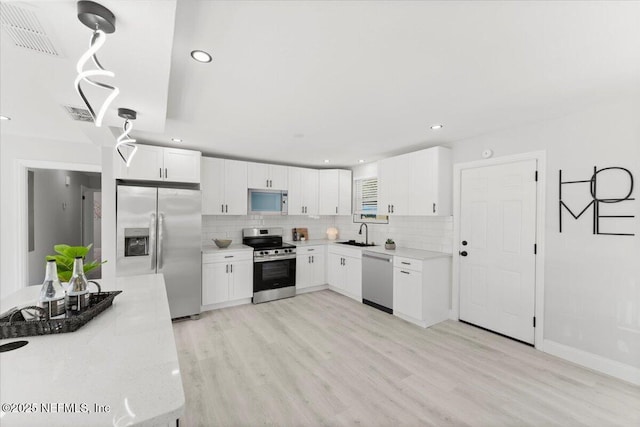 kitchen with light wood finished floors, appliances with stainless steel finishes, backsplash, and a sink