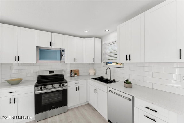 kitchen with light wood-style flooring, a sink, white cabinetry, appliances with stainless steel finishes, and decorative backsplash