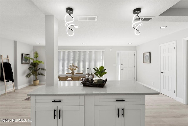 kitchen with light wood finished floors, white cabinetry, visible vents, and a textured ceiling