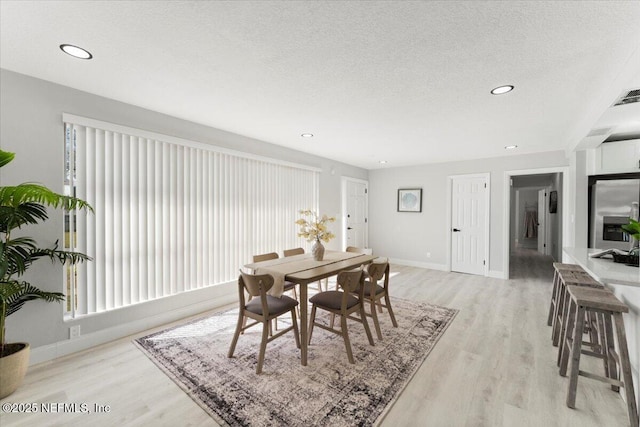 dining area with baseboards, a textured ceiling, and light wood finished floors