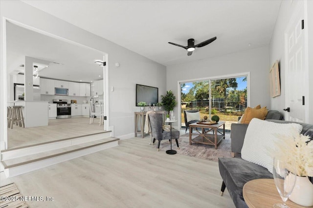 living room with light wood-style floors, ceiling fan, and baseboards