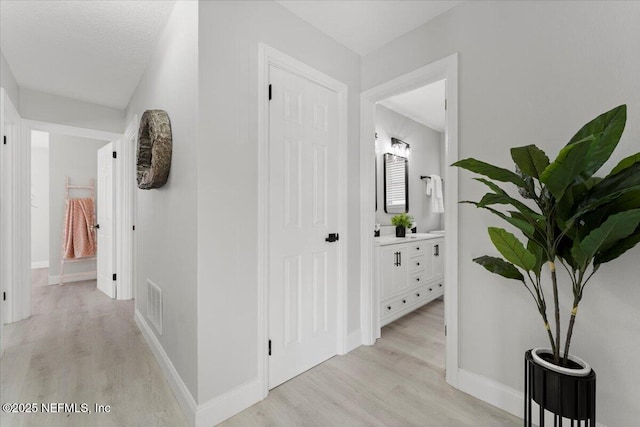 corridor with visible vents, light wood-style flooring, and baseboards