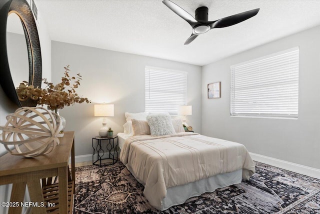 bedroom with ceiling fan, multiple windows, baseboards, and a textured ceiling