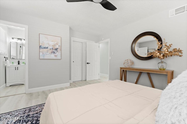 bedroom with a textured ceiling, light wood-style flooring, a sink, visible vents, and baseboards