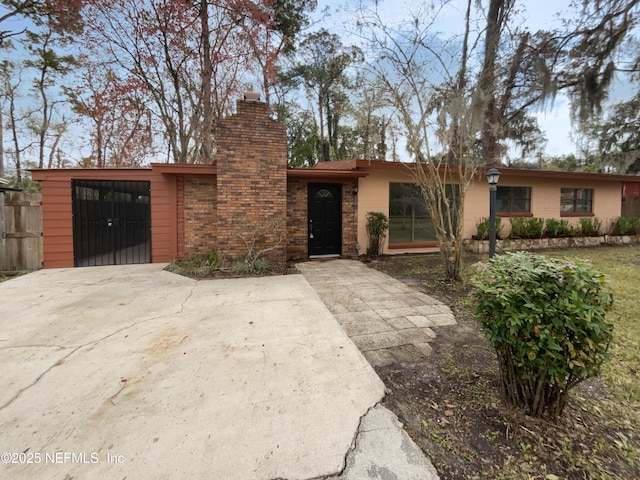 view of front of property with a garage, brick siding, fence, concrete driveway, and a chimney