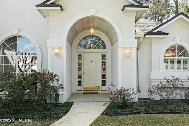 doorway to property featuring roof with shingles and stucco siding