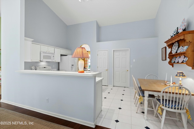 kitchen with high vaulted ceiling, white appliances, light countertops, and a peninsula