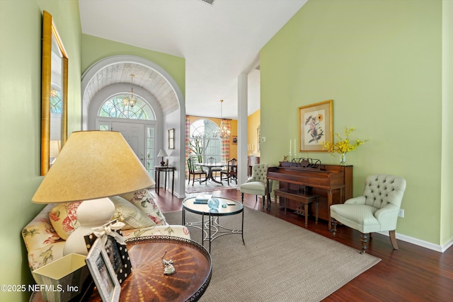 living area featuring lofted ceiling, baseboards, wood finished floors, and a notable chandelier