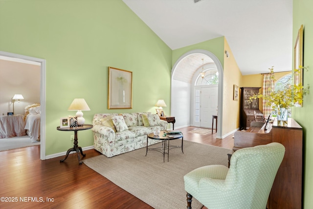 living room with high vaulted ceiling, baseboards, arched walkways, and wood finished floors