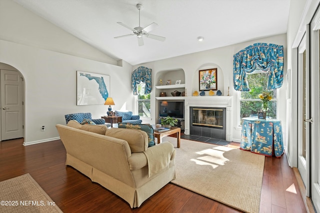 living room featuring arched walkways, built in features, a fireplace with flush hearth, dark wood-type flooring, and vaulted ceiling