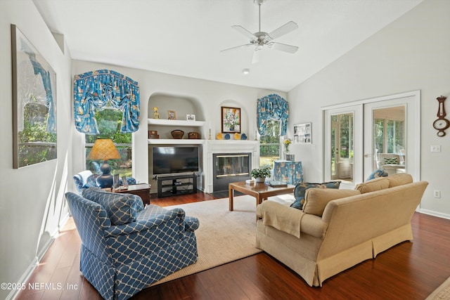 living area featuring built in shelves, french doors, lofted ceiling, a fireplace with flush hearth, and wood finished floors