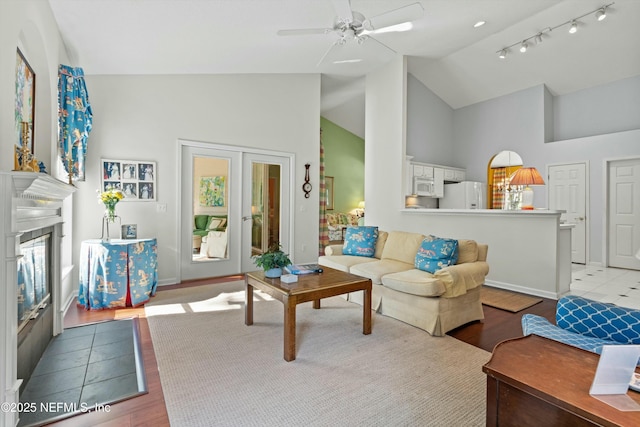 living area with baseboards, a glass covered fireplace, french doors, light wood-style floors, and high vaulted ceiling