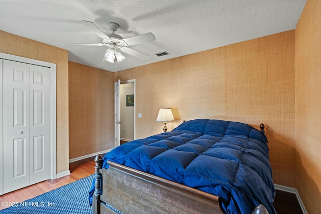 bedroom with wood finished floors, visible vents, baseboards, a closet, and wallpapered walls