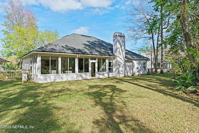 back of property with a sunroom, a lawn, a chimney, and fence