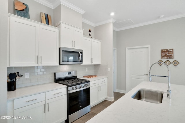 kitchen with appliances with stainless steel finishes, a sink, crown molding, white cabinetry, and backsplash