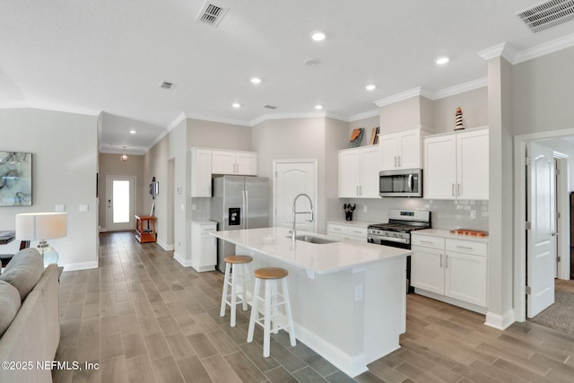 kitchen with a kitchen island with sink, stainless steel appliances, a sink, visible vents, and backsplash