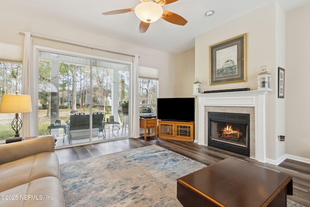 living room with a tiled fireplace, wood finished floors, a ceiling fan, and baseboards