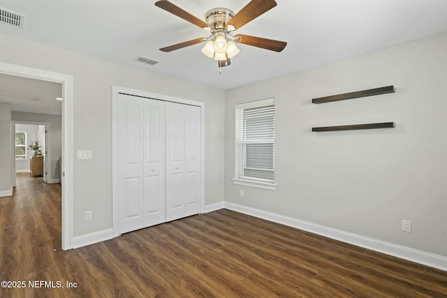 unfurnished bedroom featuring dark wood-style floors, a closet, visible vents, and baseboards