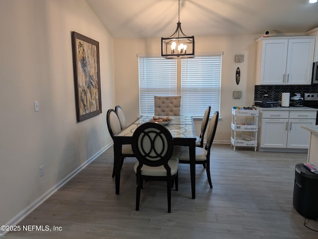 dining area featuring lofted ceiling, wood finished floors, baseboards, and an inviting chandelier