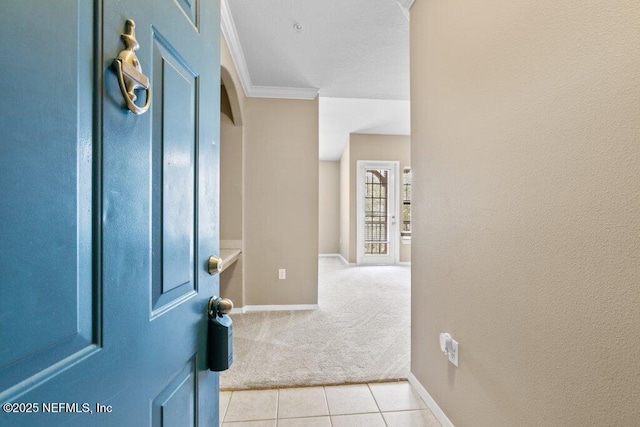 foyer entrance with light tile patterned floors, baseboards, ornamental molding, and light colored carpet