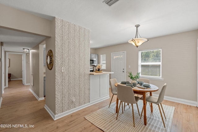 dining area featuring light wood-style floors, an accent wall, visible vents, and baseboards